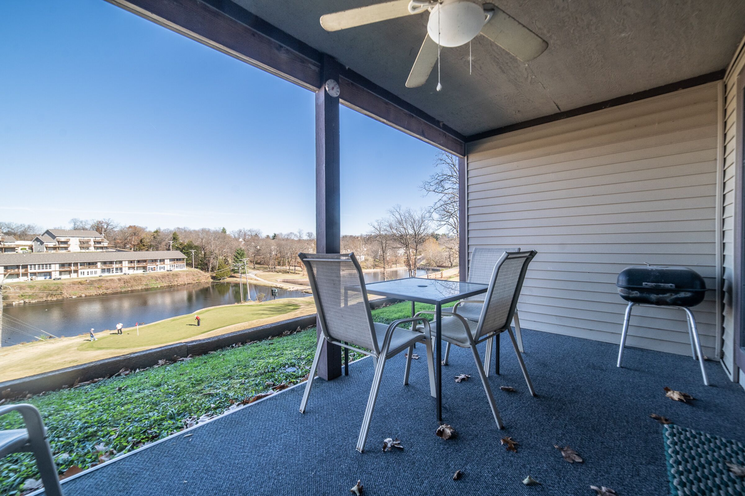 Une terrasse couverte, avec une table et des chaises, d’où l’on a vue sur une étendue d’eau et un bâtiment situé de l’autre côté.