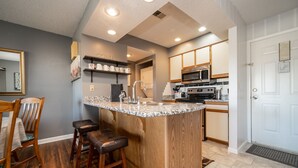 A kitchen with a central island, wooden bar stools, a microwave, oven, and a sink. - Pointe Royale Condominium Resort & Golf Course (Branson)