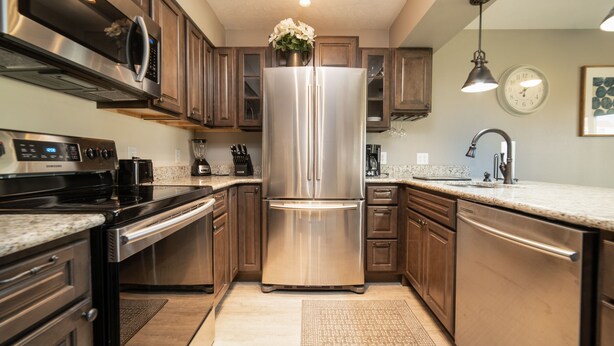 A modern kitchen with stainless steel appliances, wooden cabinets, granite countertops, and a central island. - Pointe Royale Condominium Resort & Golf Course (Branson)
