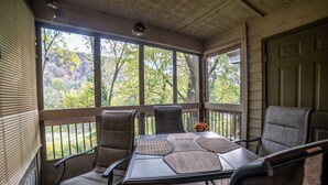 A covered patio with a table and four chairs, large windows, and a view of trees. - Pointe Royale Condominium Resort & Golf Course (Branson)