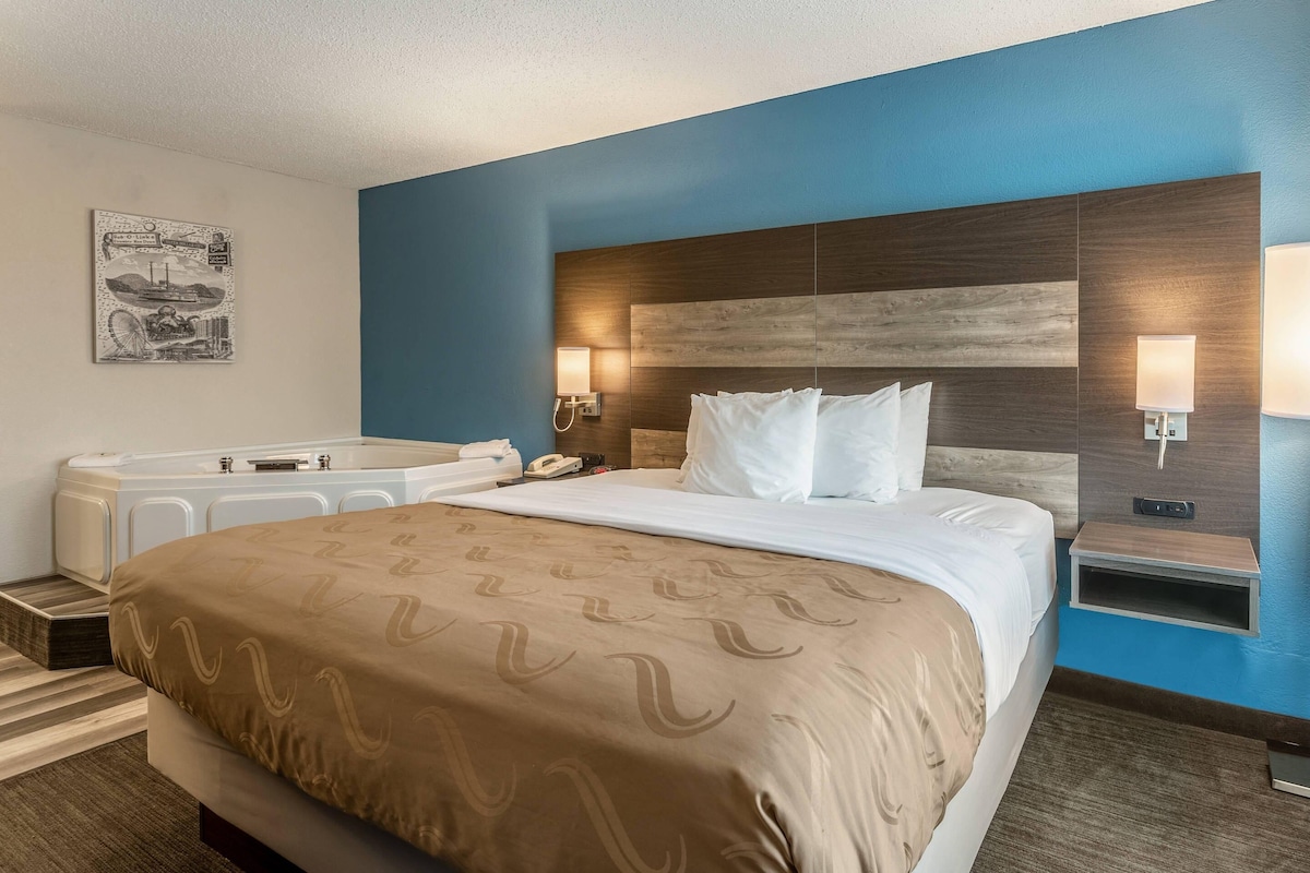 A hotel room with a bed, a bathtub, and a wall-mounted phone.
