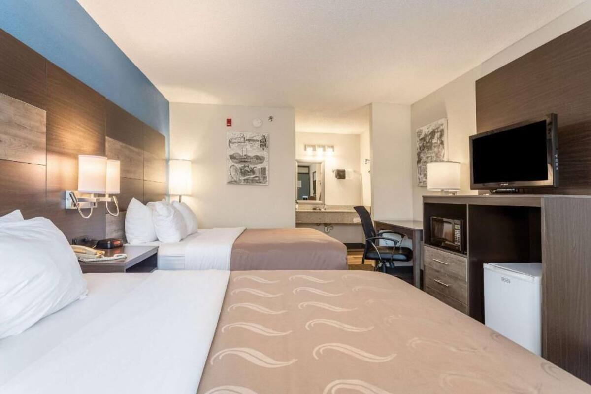 A hotel room with two beds, a desk, a chair, a TV, a microwave, and a refrigerator.