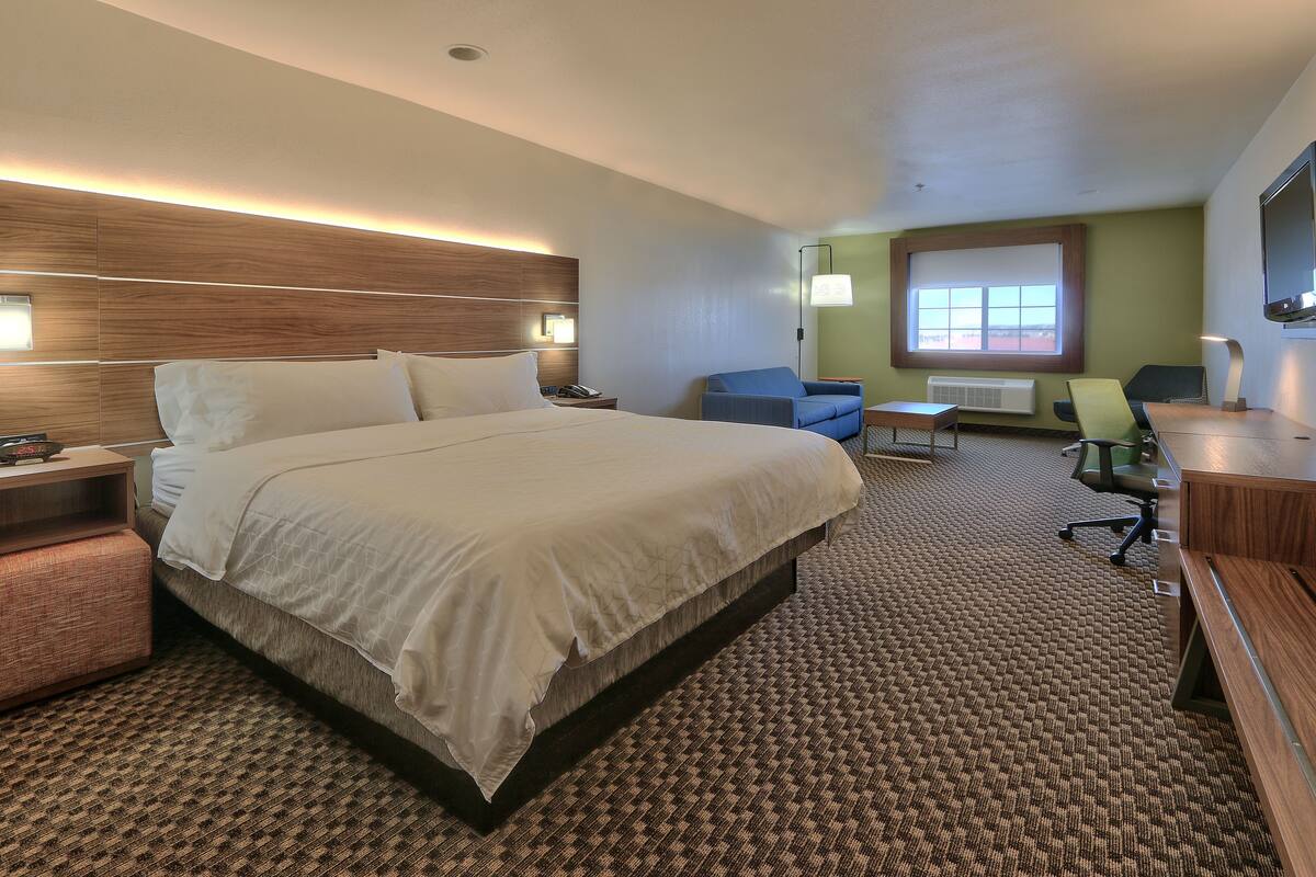 A hotel room with a large bed, a desk, a chair, and a small table.