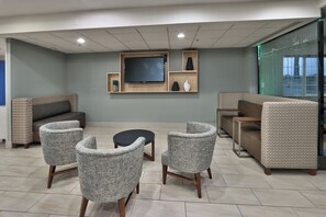 A modern waiting area with a flat-screen TV mounted on the wall, a sofa, and patterned armchairs.