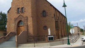 Una iglesia con un campanario alto, una puerta de madera y una estatua en primer plano.
