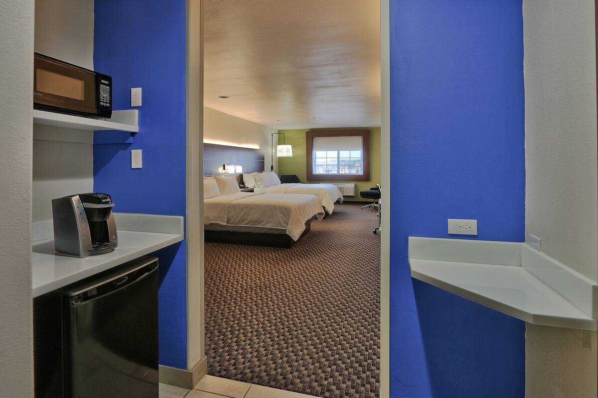 A hotel room with a microwave on a shelf, a coffee maker, a bed, and a desk.