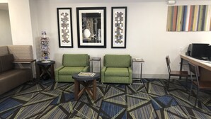 A hotel lobby with a patterned carpet, two green armchairs, a sofa, a small round table, a bookshelf, and three framed artworks on the wall. - Holiday Inn Express SANTA ROSA by IHG (Santa Rosa)