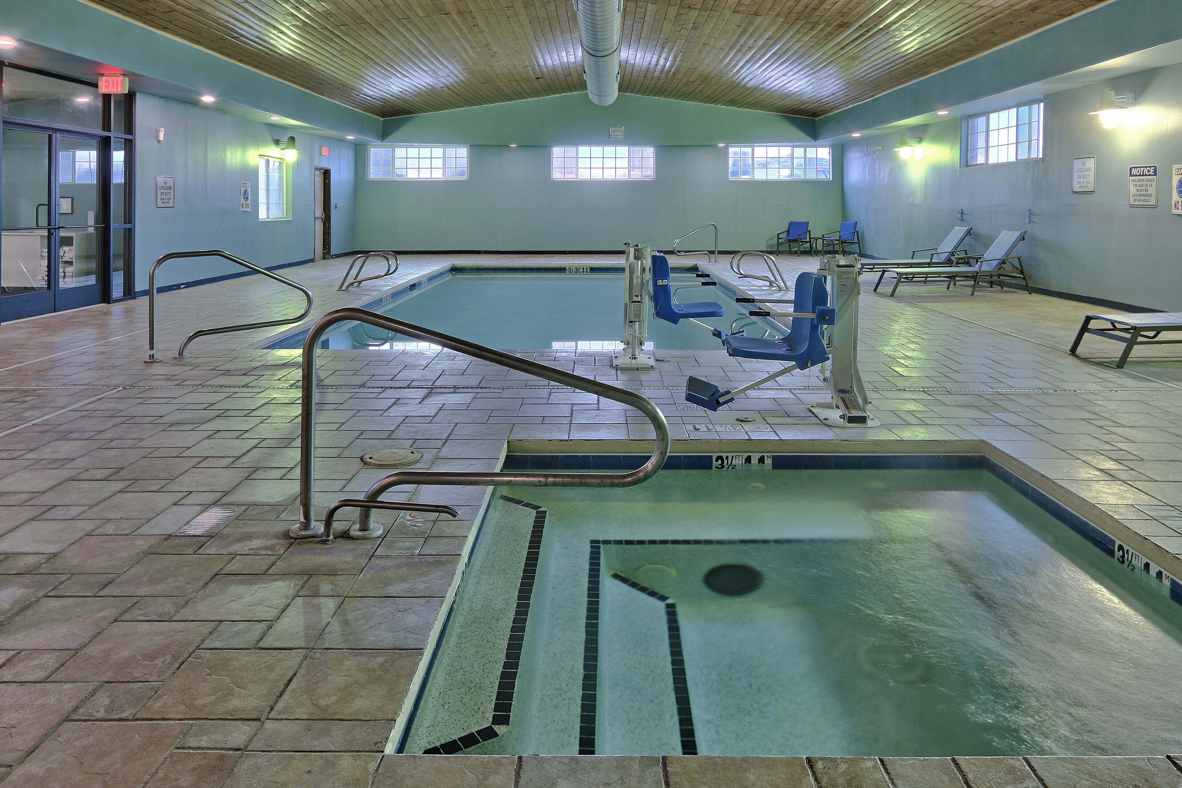 An indoor swimming pool with multiple lanes, safety railings, and lounge chairs.