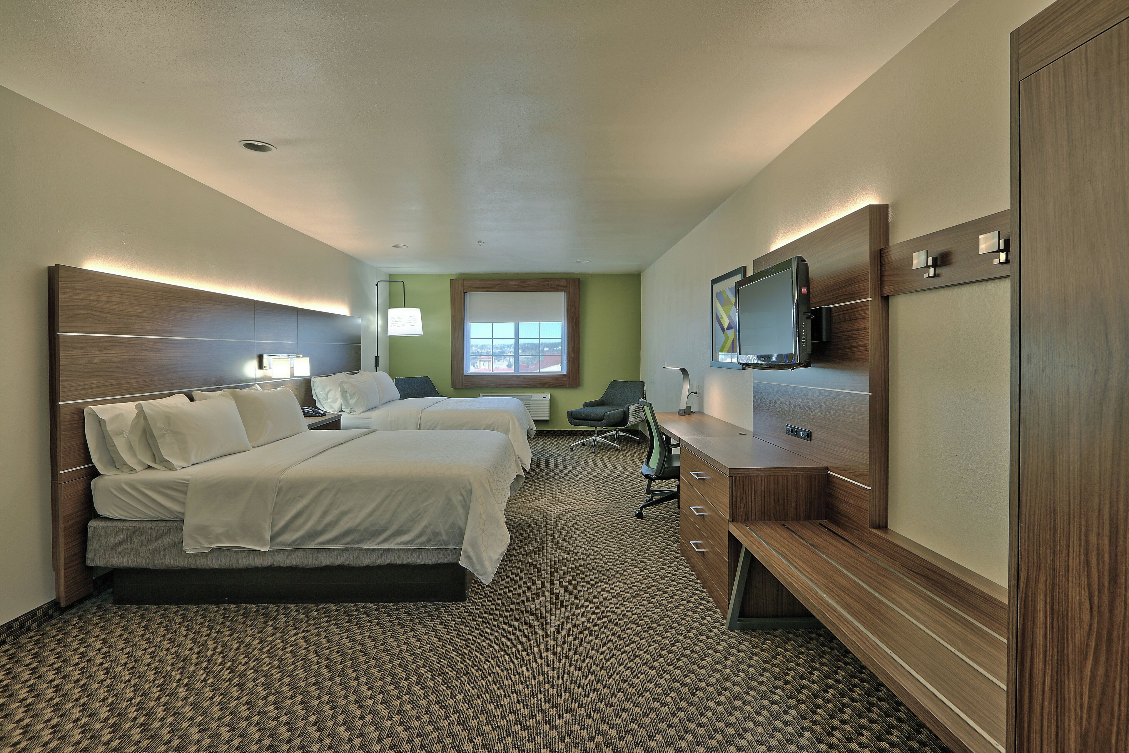 A hotel room with two beds, a desk, a TV, and a window with a view.
