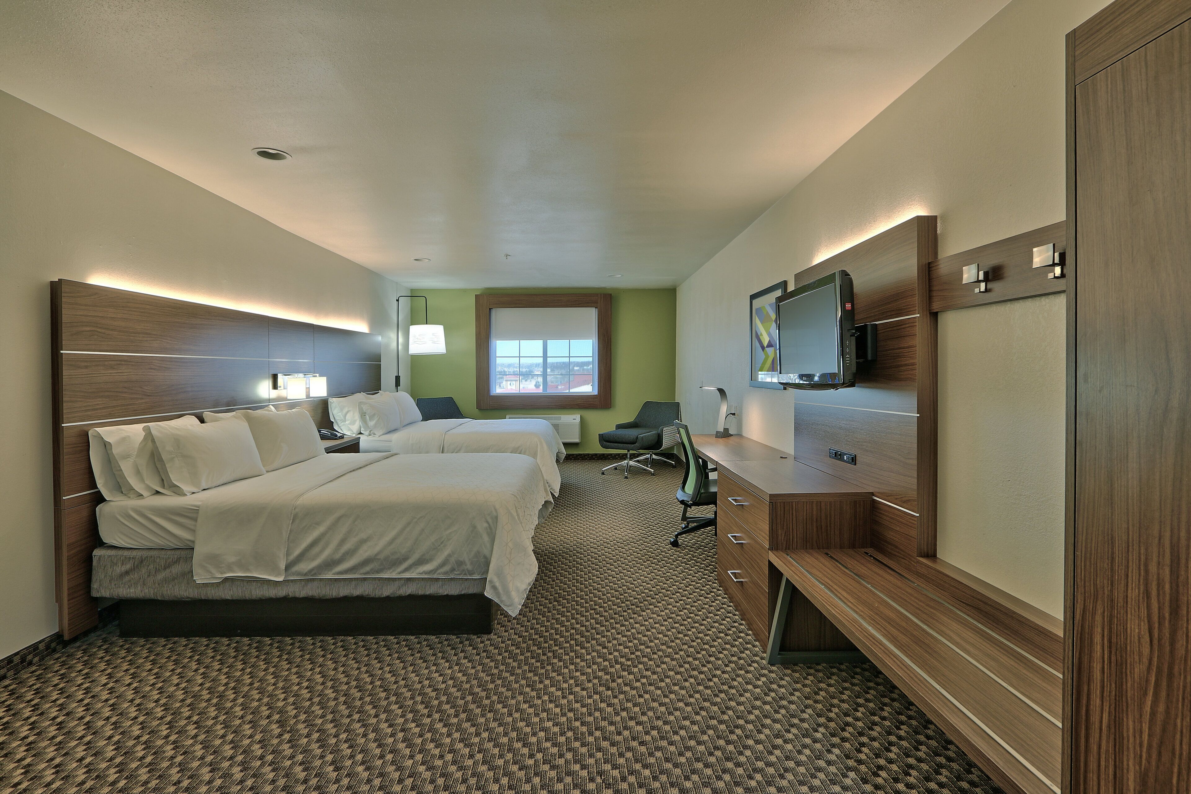 A hotel room with two beds, a desk, a television, and a window with a view.