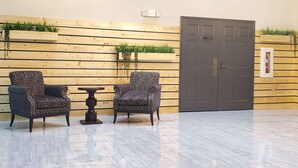Une pièce avec deux fauteuils à motifs, une petite table, un mur en bois orné de plantes et une porte fermée.