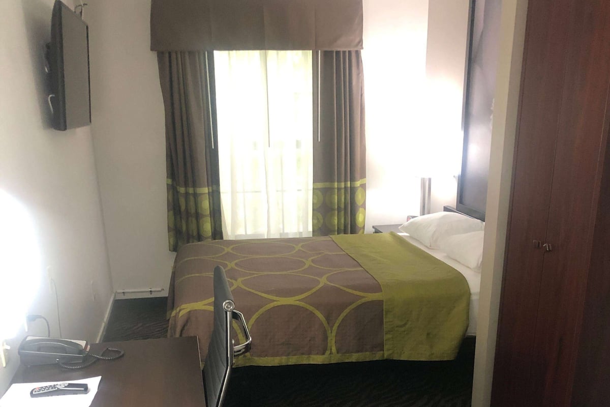 Ein Hotelzimmer mit Bett, Vorhängen, Schreibtisch und Telefon sowie einem Fernseher an der Wand.