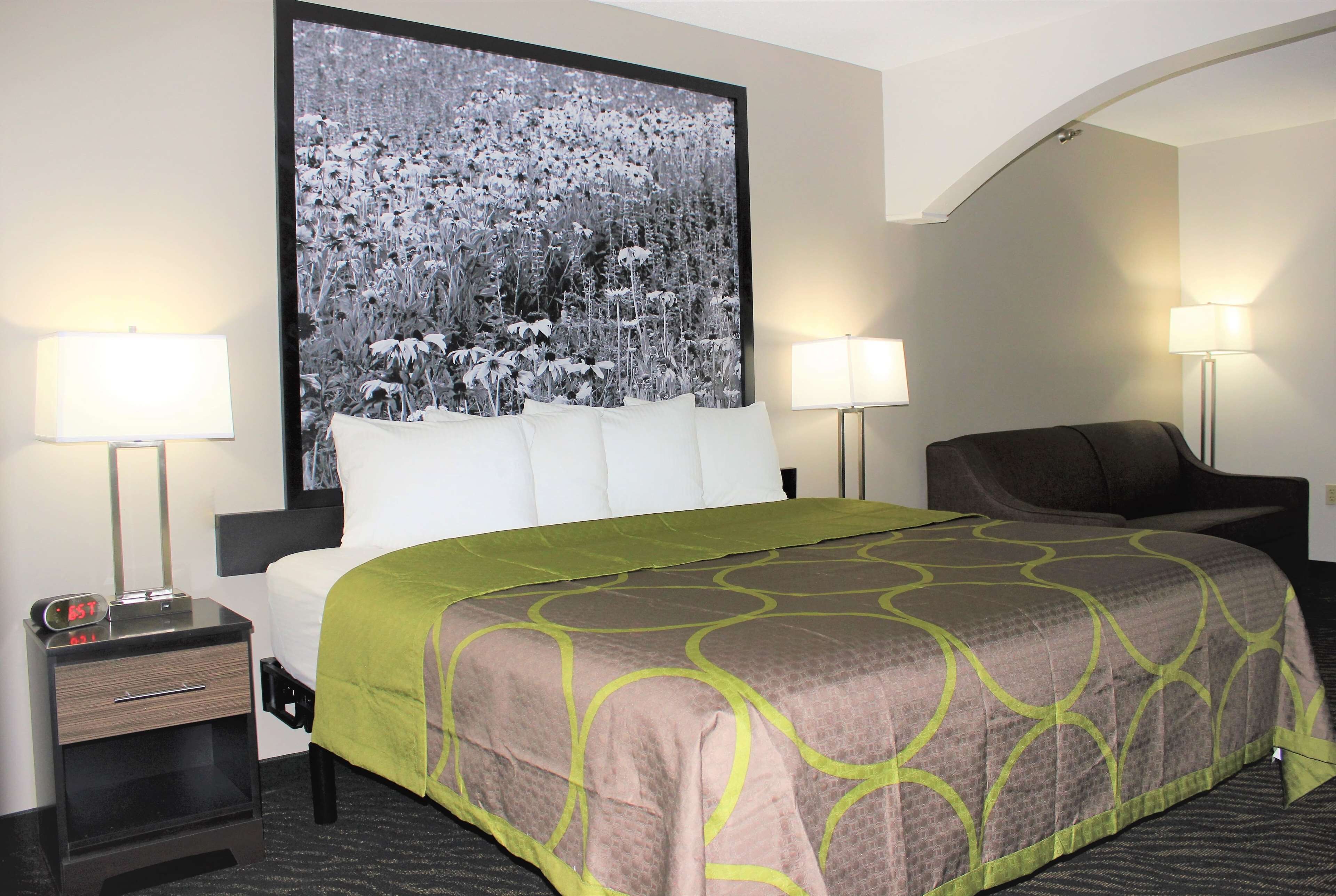 A hotel room with a large bed, two bedside tables, a chair, and a large wall-mounted picture.