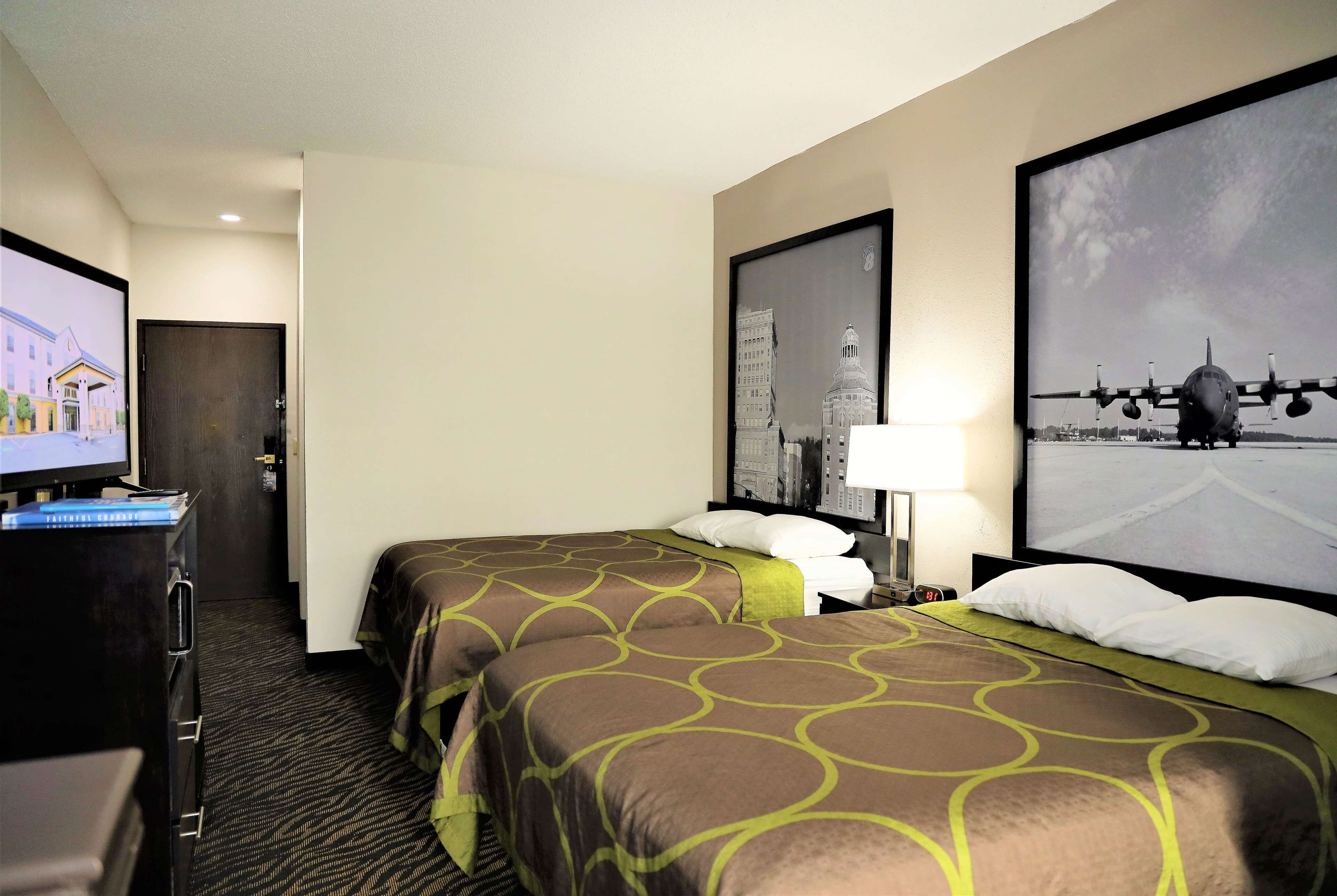 A hotel room with two beds, a TV, a desk, and a large window with a cityscape view.