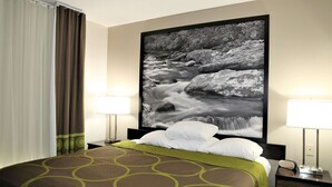 Une chambre d’hôtel avec un grand lit, deux lampes de chevet, une table de nuit, une horloge numérique et une grande photographie encadrée représentant une cascade, accrochée au mur.