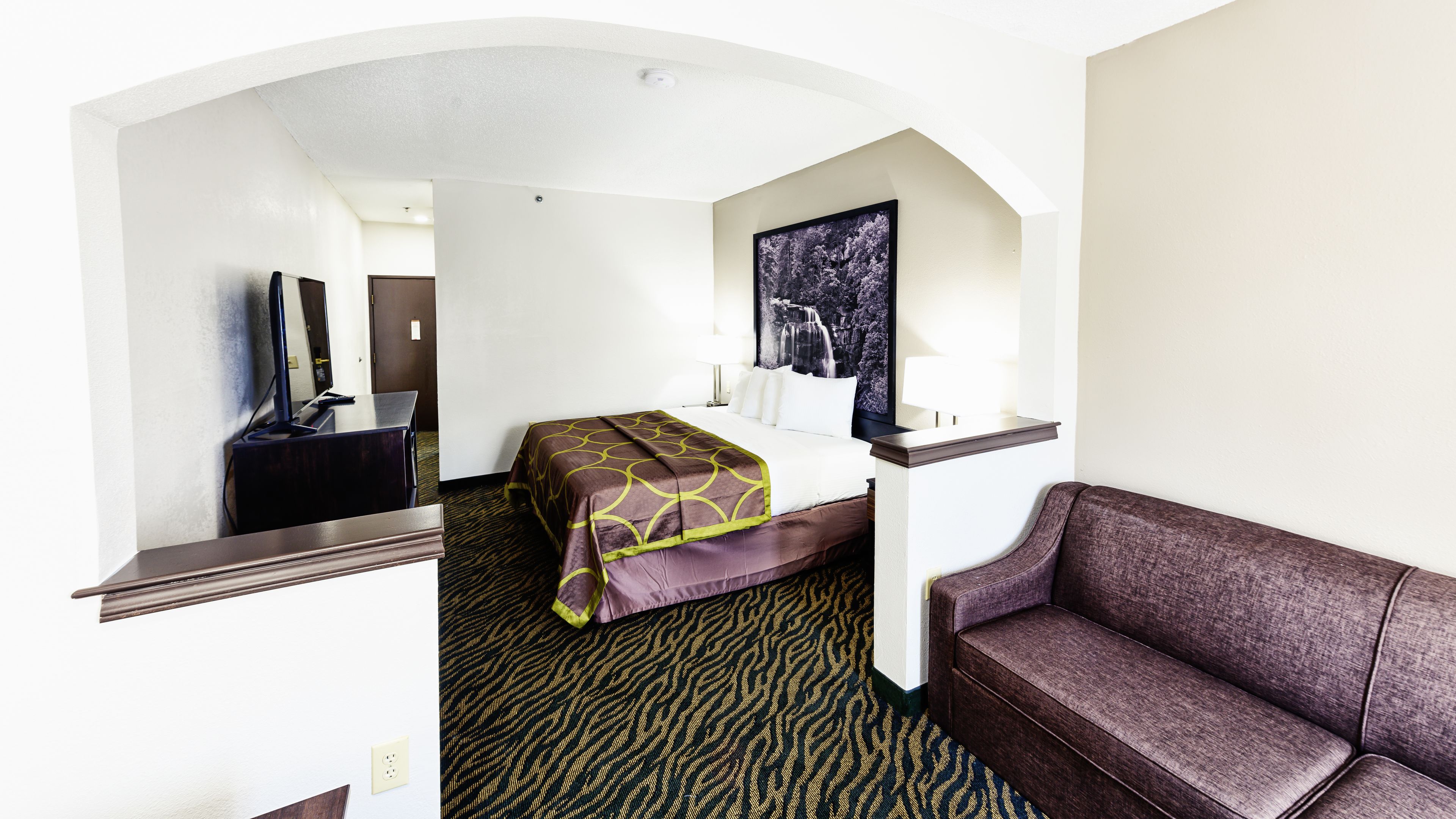 Une chambre d’hôtel avec un lit, un bureau, une chaise, un canapé, un tableau et un miroir.