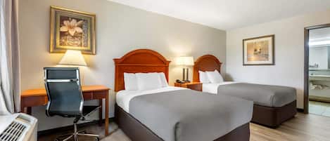 A hotel room with two beds, a desk, a chair, and a desk lamp.