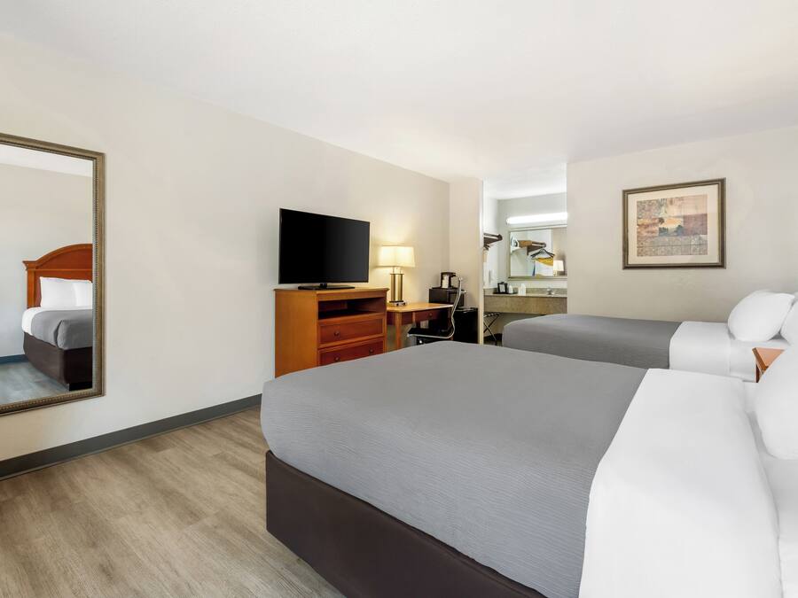 A hotel room with two beds, a television, a desk, and a mirror.
