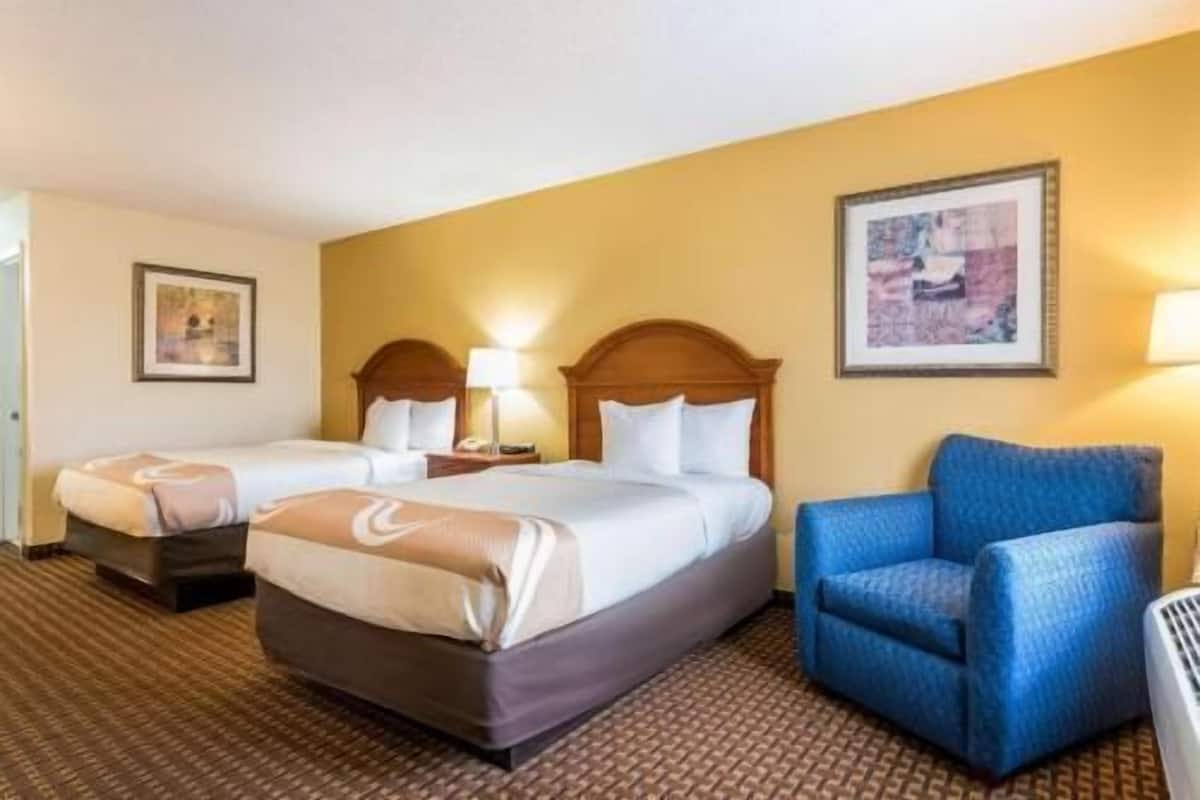 A hotel room with two beds, a blue armchair, and a framed picture on the wall.