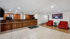 A reception area with a wooden reception desk, two red chairs, a flat-screen TV, and a framed picture on the wall. - Quality Inn Battleboro - Rocky Mount (Battleboro)