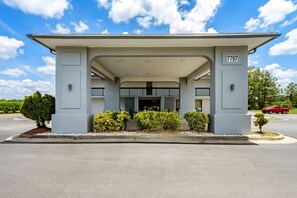 A modern building with a covered entrance, numbered 7797, featuring a symmetrical facade, a central entrance, and a parking area in front.