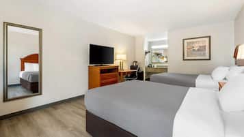 Une chambre d’hôtel avec deux lits, une télévision, un bureau avec une lampe et un miroir.