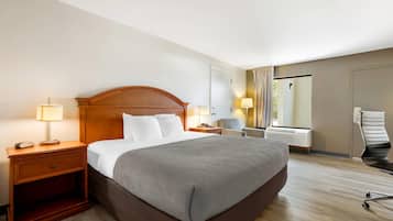 Ein Hotelzimmer mit einem großen Bett, Nachttischlampen, einem Sessel, einem Schreibtisch und einem Fenster mit Vorhängen.