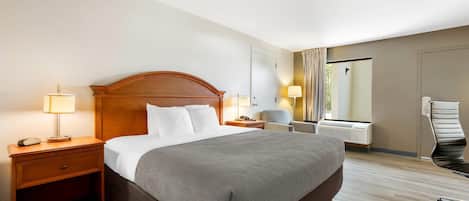 Habitación de hotel con una cama grande, lámparas de noche, una silla, un escritorio y una ventana con cortinas.