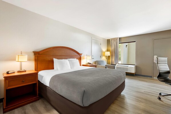 A hotel room with a large bed, bedside lamps, a chair, a desk, and a window with curtains.