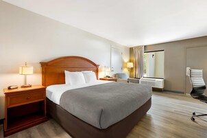Habitación de hotel con una cama grande, lámparas de noche, una silla, un escritorio y una ventana con cortinas.