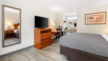 A hotel room with a bed, a desk with a computer, a television, a mirror, and a framed picture on the wall.