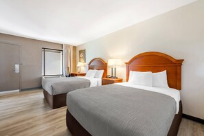Habitación de hotel con dos camas, una puerta, un ventanal y una obra de arte colgada en la pared.