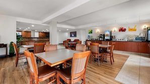 Un comedor de hotel con mesas y sillas de madera, una zona de cocina con electrodomésticos y vistas al exterior.