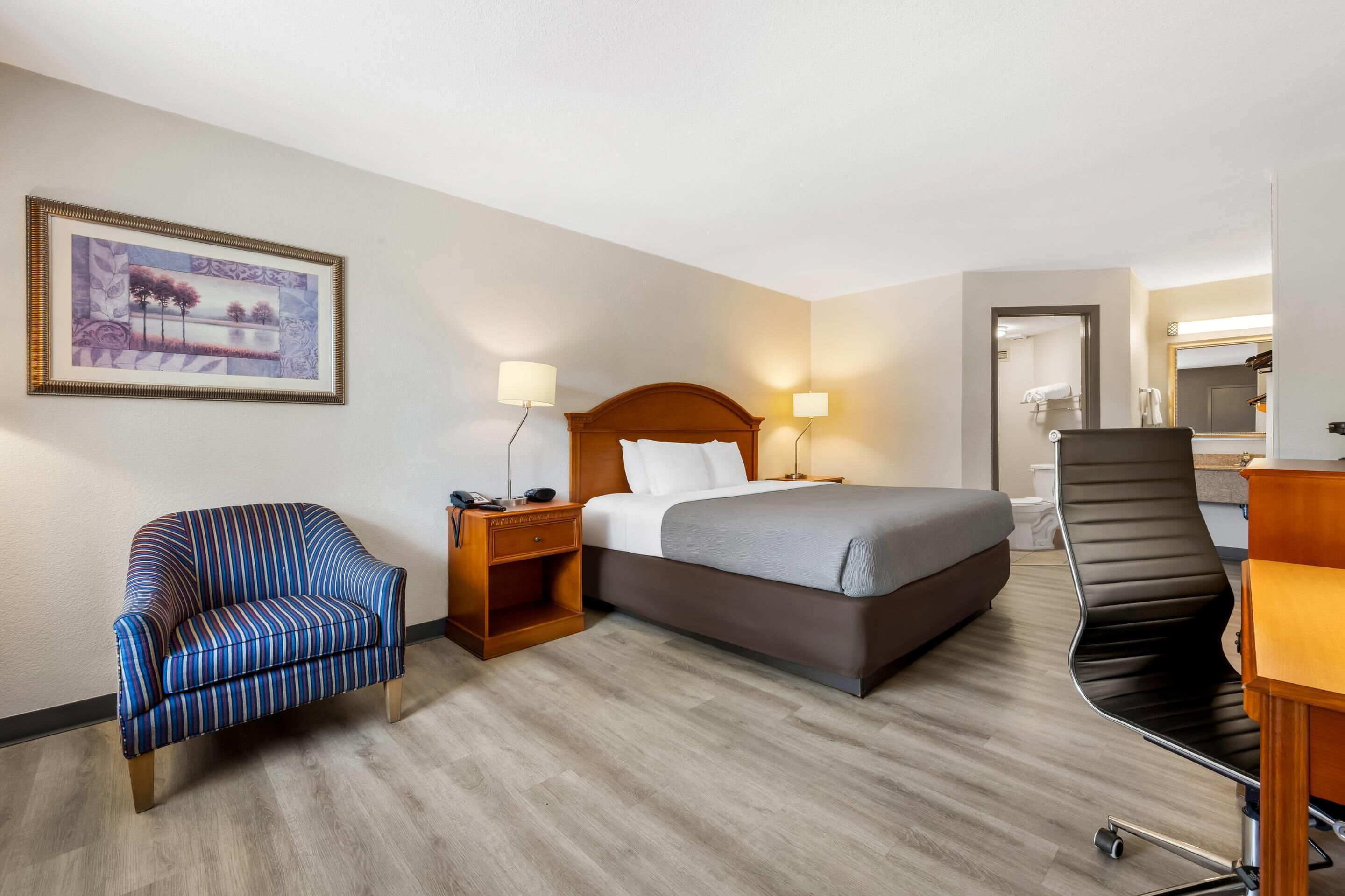 A hotel room with a bed, a chair, a desk, and a bathroom visible through an open door.