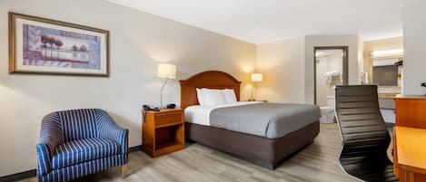 A hotel room with a bed, a chair, a desk, and a bathroom visible through an open door.