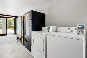 A laundry room with a front-loading washer and dryer, a wall-mounted dryer, and a vending machine.