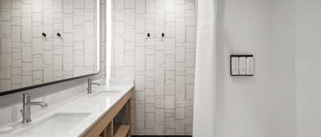 Un baño moderno con lavamanos de mármol, tocador de madera, ducha con cortina blanca y azulejos con diseño.