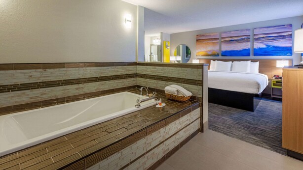 A modern hotel bathroom with a large bathtub, a separate shower area, and a bed with a view of the cityscape. - Days Inn by Wyndham Sturtevant / Racine / Mount Pleasant (Mount Pleasant)
