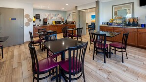 A hotel dining area with multiple tables and chairs, a kitchen in the background, and a buffet counter with various food items. - Days Inn by Wyndham Sturtevant / Racine / Mount Pleasant (Mount Pleasant)