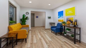 A modern lobby with a yellow sofa, a blue armchair, and a wooden floor. There are wall-mounted mirrors, a console table with plants, and framed pictures. - Days Inn by Wyndham Sturtevant / Racine / Mount Pleasant (Mount Pleasant)