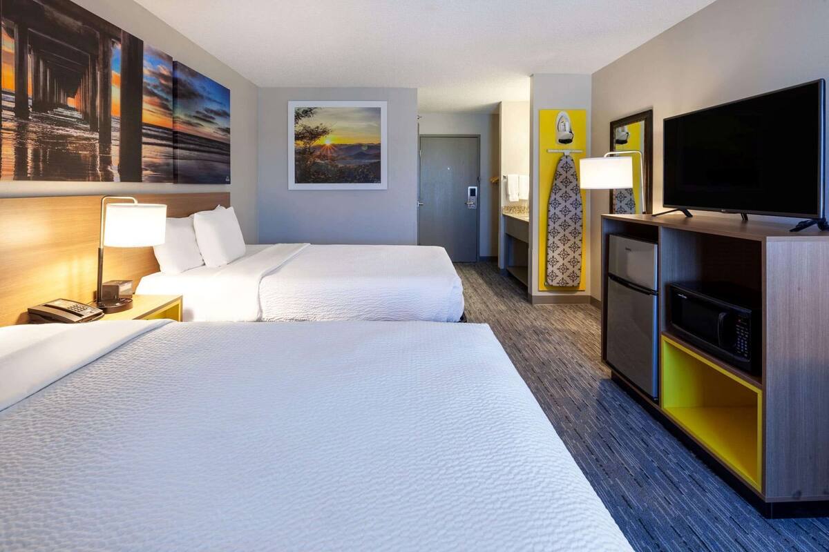 Une chambre d’hôtel avec deux lits, une télévision, un bureau avec une lampe et des œuvres d’art accrochées aux murs.