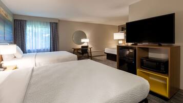 A hotel room with two beds, a desk with a chair, a flat-screen TV, a microwave, and a large window with curtains.