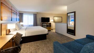 A hotel room with a bed, a desk with a chair, a TV, a sofa, and a large mirror.