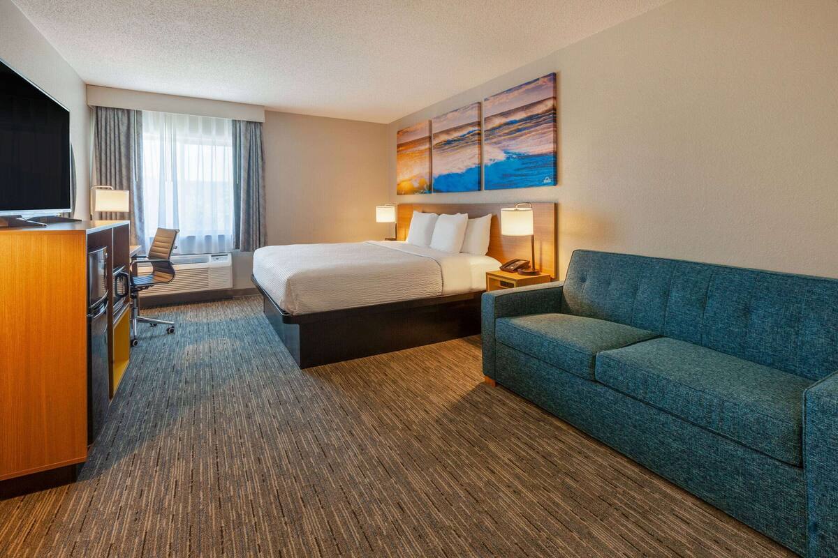 Une chambre d’hôtel avec un lit, un bureau équipé d’un ordinateur, un canapé bleu et un tableau accroché au mur.
