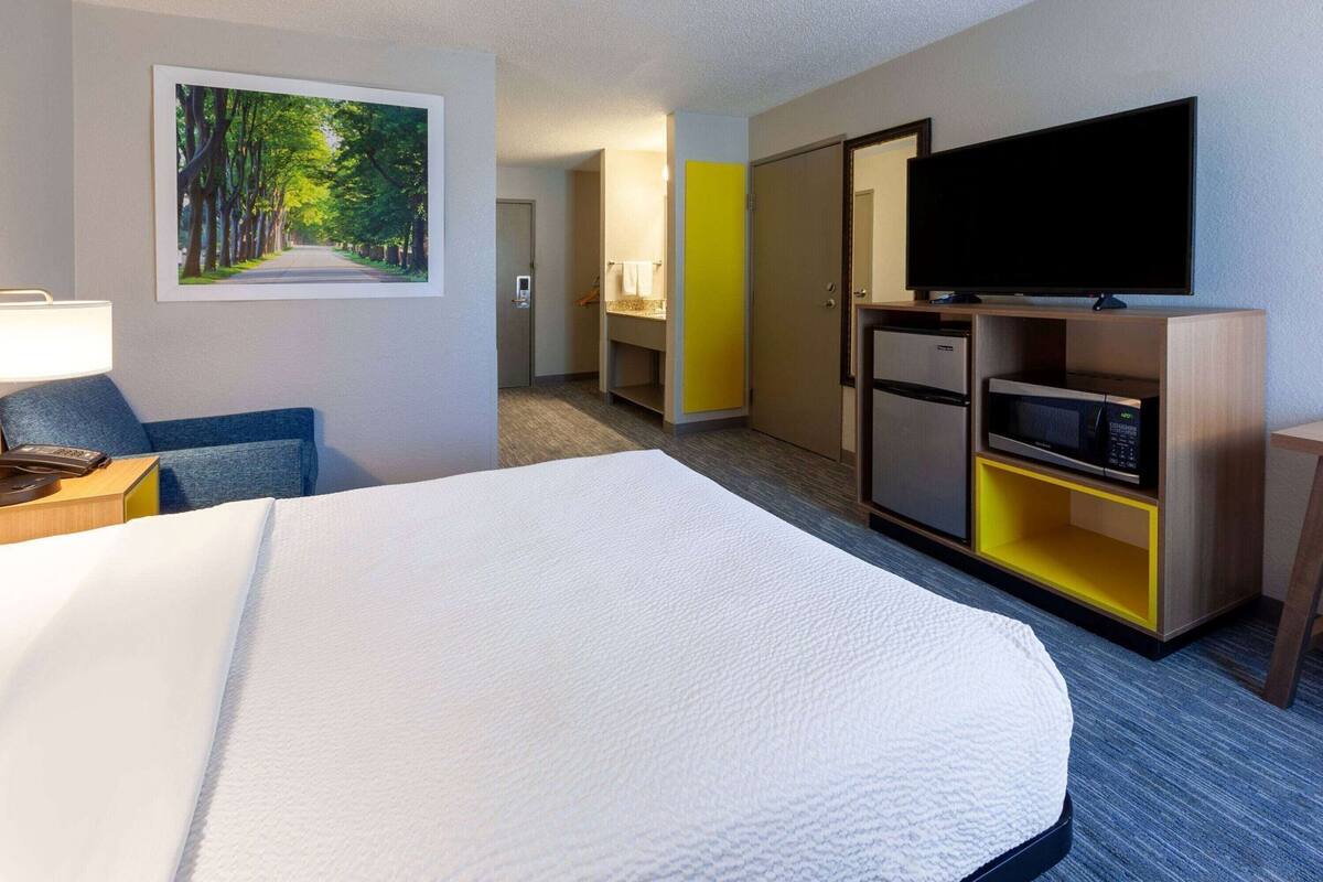 Une chambre d’hôtel avec un lit, une télévision, un four à micro-ondes et une salle de bain que l’on aperçoit à l’arrière-plan.