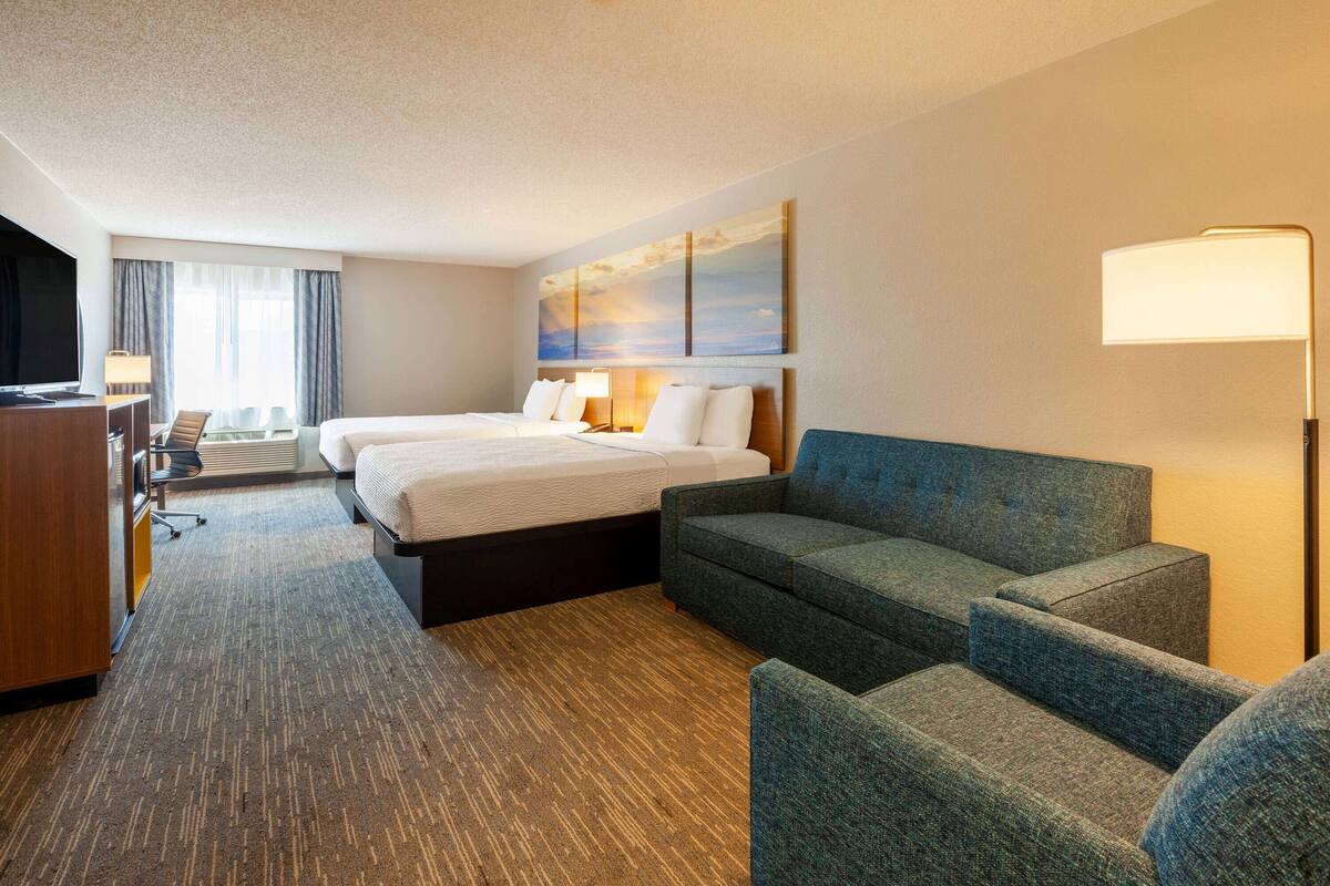 Une chambre d’hôtel avec deux lits, un bureau, une télévision et un canapé.