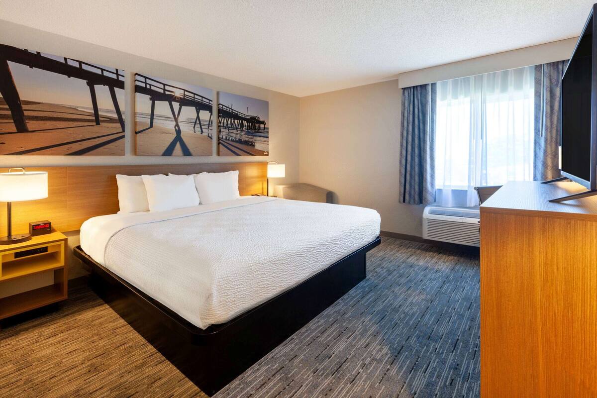 Une chambre d’hôtel avec un grand lit, un bureau, un téléviseur à écran plat, une fenêtre avec des rideaux et des œuvres d’art accrochées au mur.