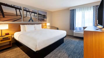 A hotel room with a large bed, a desk, a flat-screen TV, a window with curtains, and artwork on the wall.