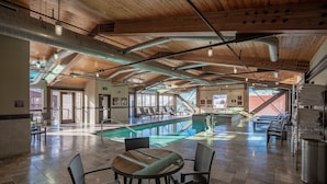 Uma área interna de piscina espaçosa, com teto de madeira, mesa de bilhar e assentos de estar.