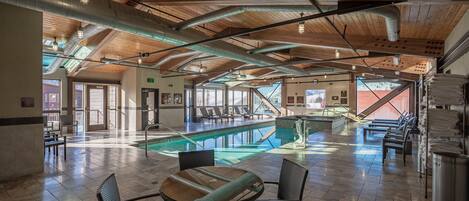 A spacious indoor pool area with a wooden ceiling, a pool table, and lounge seating.
